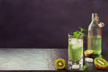 Tropical summer kiwi fruits and kiwi smoothies fermented juice cocktail with chia seeds in glass and bottle on dark copy space background.