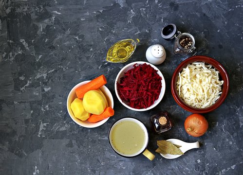 Ingredients for cooking borscht, traditional hot Russian soup with beetroot, cabbage and potatoes on a dark gray concrete background.