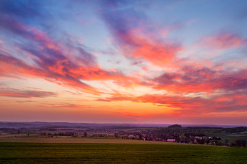 red sunset clouds over fresh green field with grass