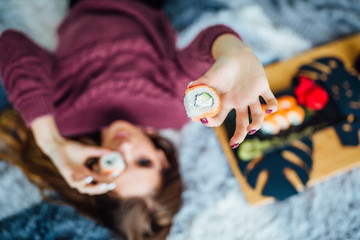 Focus at sushi roll. Young girl lying in bed with food