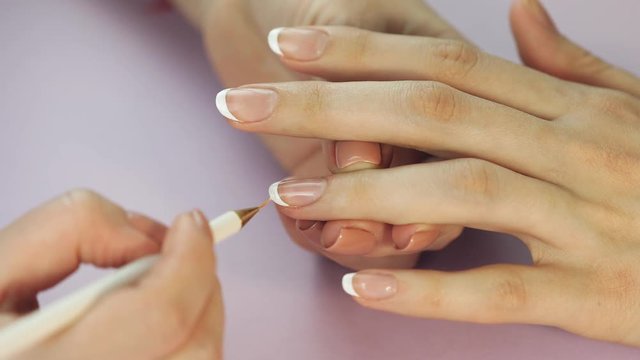 the manicurist paints the client's nails with  nail polish on a lite purple background Painting nails. Female hands with beautiful french manicure