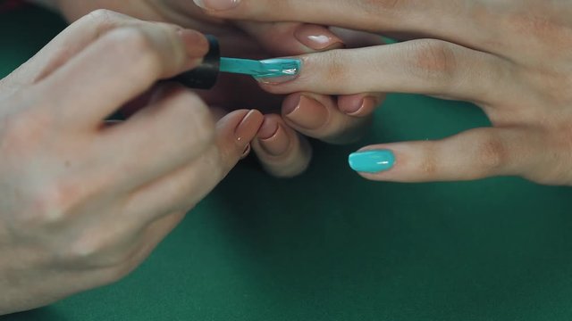 the manicurist paints the client's nails with green nail polish on a green background Painting nails.