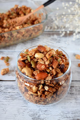 Granola with different nuts in a glass jar on the white wooden table
