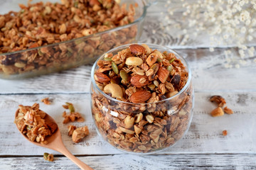 Granola with different nuts in a glass jar on the white wooden table