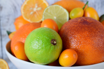Citrus assortment in a bowl against the white wooden background. Red orange, lime, lemon and kumquats