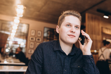 Handsome brutal business man student sitting in cafe drinking coffee in the morning, calling by smartphone. Breakfast,  business, technology concept