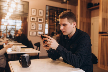 Handsome brutal business man student sitting in cafe drinking coffee in the morning, chating in social network by smartphone. Breakfast, business, technology concept
