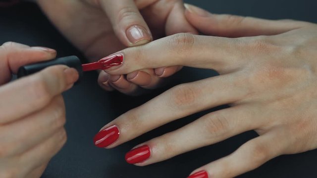 the manicurist paints the client's nails with red nail polish on a black background Painting nails.