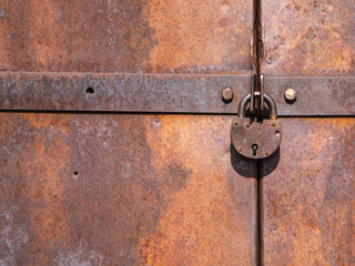 Old lock hangs on metal doors covered in rust.
