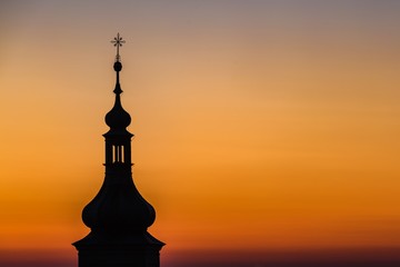 Dark silhouette of church tower of Our Lady Victorious and the Prague Infant Jesus in Prague, Czech Republic. Morning dawn sky with orange, yellow, pink and violet colors.