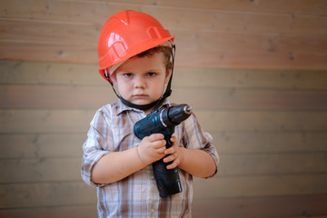 cute boy in a construction helmet and glasses with a screwdriver in his hands in the interior of a wooden house