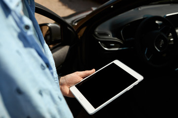 Close up shot of generic portable electronic device in man's hands. Unrecognizable male sitting in car with digital tablet with blank display using online map or GPS navigation. Auto computer service