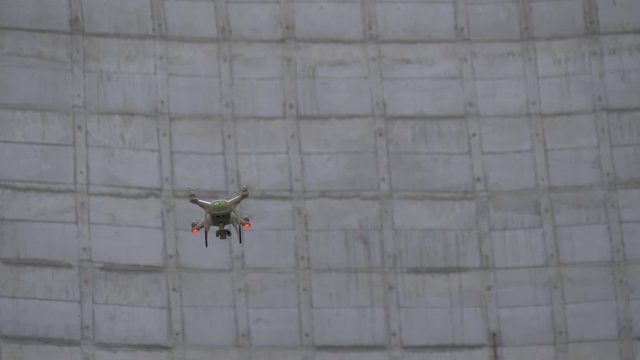 Drone tracking at a construction site. Drone flies between building structures. Drone is involved in the construction of industrial buildings. Drone flies against a concrete wall.