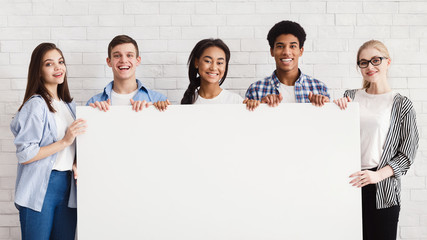 Happy teenagers holding empty banner, white brick wall