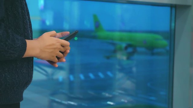 daughter traveler with a backpack airplane flights airport concept. girl teenager with a smartphone looks out the window at the airport area airplanes at a distance. teen lifestyle girl looks at the