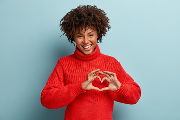 Portrait of lovely female model makes heart gesture, says be my valentine, demonstrates love sign,...