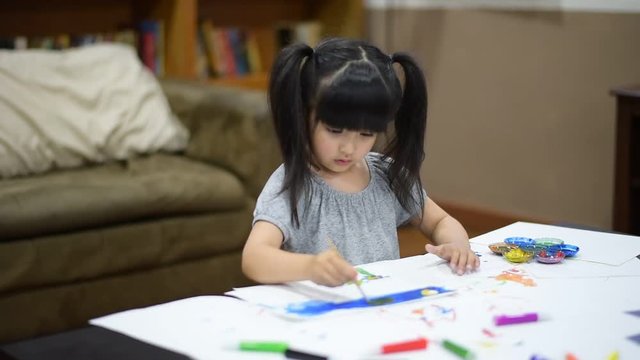 Cute little girl create art on paper with colored paint on the table in front of sofa  at home. Concept of education.