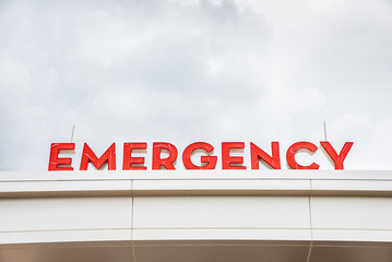 A prominent red 3D all-caps lighted emergency directional sign and marker perched on the awning and canopy of the main hospital entrance.