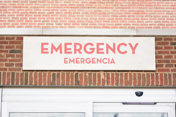 A prominent red emergency room signage with foreign language translation atop the automatic door entrance of a hospital facility.