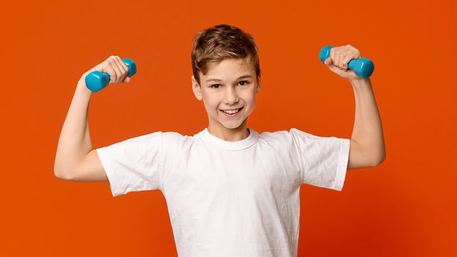 Strong little man exercising with dumbbells, orange background