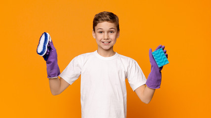 Cute teen boy in rubber gloves holding sponge and brush © Prostock-studio