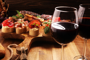 Traditional italian antipasto bruschetta appetizer with cherry tomatoes, cream cheese, basil leaves and balsamic vinegar on cutting board with prosciutto, salami, cheese
