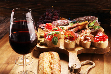 Traditional italian antipasto bruschetta appetizer with cherry tomatoes, cream cheese, basil leaves and balsamic vinegar on cutting board with prosciutto, salami, cheese