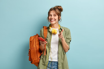 Photo of delighted European woman points at you happily, holds smartphone device connected to...