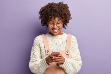 Indoor shot of happy curly woman with pleased facial expression, reads nice message from boyfriend,...