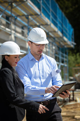 Two architects a man and a woman in construction in white helmets.