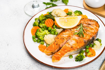 Grilled salmon steak with vegetables on white.