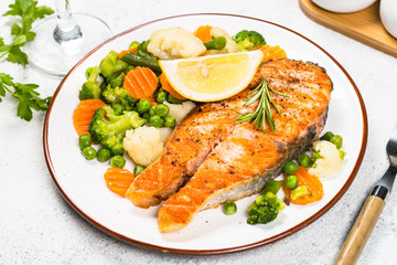 Grilled salmon steak with vegetables on white.