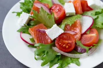 Fresh salad from salmon and vegetables on a white plate.
