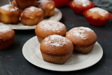 Homemade muffins with pineapple pieces, sprinkled with powdered sugar, are located on a dark background