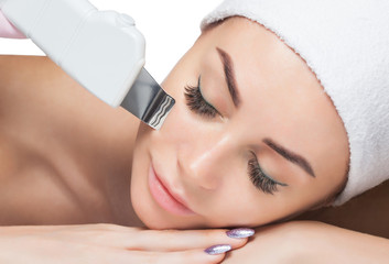 The doctor-cosmetologist makes the ultrasound cleaning procedure of the facial skin of a beautiful,...