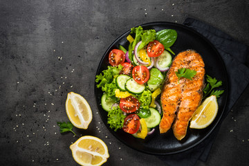 Grilled salmon fish steak with vegetables on black.