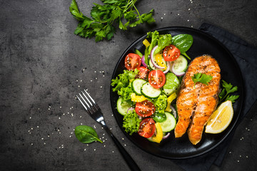 Grilled salmon fish steak with vegetables on black.