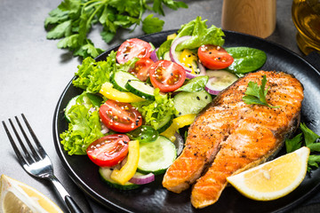 Grilled salmon fish steak with vegetables on black.