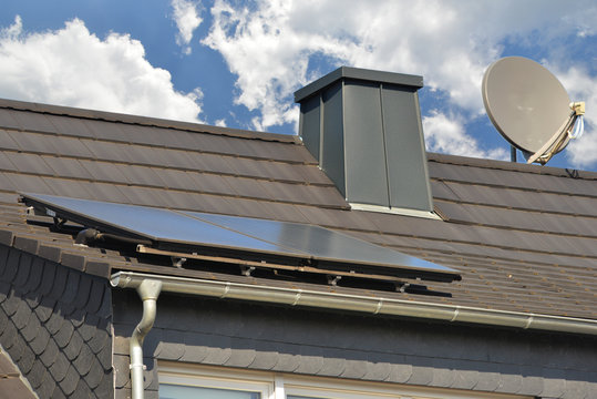 Solaranlage mit Metall verkleideter Schornstein und Satelitenantenne auf dem Ziegeldach eines Wohngebäudes