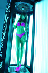 Young beautiful sexy brunette woman in violet bikini standing and tanning in solarium ultraviolet...