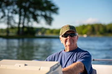 A senior man enjoys driving a boat on a beautiful lake on a sunny day.