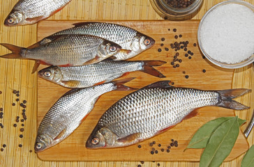 Fresh river fish roach with spices salt, pepper, bay leaf on a cutting wooden board.