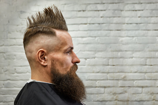 portrait of a man with a mohawk and beard in a barber chair against a brick wall. close up, brick background, copy space
