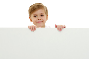 A little boy is looking from behind an empty banner.