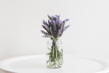 Close up of lavender in glass jar on small table against neutral wall background - matte filter...