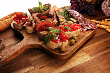 Traditional italian antipasto bruschetta appetizer with cherry tomatoes, cream cheese, basil leaves and balsamic vinegar on cutting board with prosciutto, salami, cheese