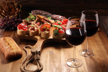 Traditional italian antipasto bruschetta appetizer with cherry tomatoes, cream cheese, basil leaves and balsamic vinegar on cutting board with prosciutto, salami, cheese