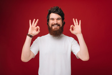 A handsome bearded man in white tshirt over red  background showing ok sign