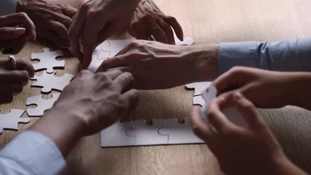Diverse hands of business people connect puzzle together on desk