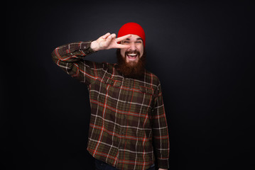 Portrait of bearded man doing pace sign  in front of eye over dark background